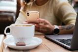 A woman with a tattoo on her arm typing on her mobile phone with a coffee and a chocolate