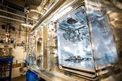 A technician in a white cleansuit makes adjustments inside a large piece of metal scientific equipment