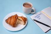 A croissant and a mug of hot chocolate with a pen and notebook which says Chemistry Revision