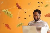 A man holding a laptop and some files smiles as he looks down at his computer. He is surrounded by illustrations of autumn leaves being blown in the wind. 