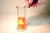 A photograph showing a glass container as potassium iodide solution is added to a lead nitrate solution, leading to an yellow-orange precipitate being formed