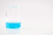 Blue copper(II) sulfate solution in a glass beaker against a neutral grey-white background