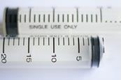 A close-up photograph of two large disposable plastic syringes against a plain white-grey background