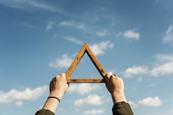 two hands holding a wooden triangle up to a blue sky with clouds in it