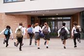 Young high school students in school uniform carrying backpacks run towards the school entrance.