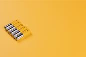 Five silver and yellow AA alkaline batteries against a yellow background