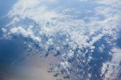 An aerial photograph of cumulus clouds above the sea, with shadows and a ship visible below
