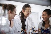 A chemistry teacher in a lab coat speaking with two students