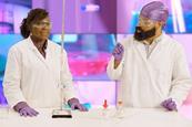 Two people in lab coats, safety goggles and latex gloves performing a titration