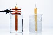 A photograph of two sealed ampoules containing nitrogen dioxide; one is dark brown in colour, in a beaker of hot water, and one is light brown, in a beaker of ice water.