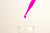 pink drop of liquid falling from pipette into flask