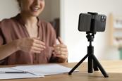 A woman recording herself explaining something on a mobile phone that's sitting on a tripod