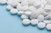 A close-up photograph of a pile of white aspirin pills on a blue paper background