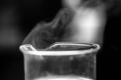 A photograph of a glass beaker containing a liquid, with a gas visibly rising from the top
