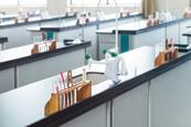 A school lab with no people but each station has equipment ready for a practical lesson including test tubes in a rack, with a holder and brush as well as a stirrer and pipette