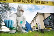 A crime scene technician wearing white overalls and latex gloves collects evidence from a lawn with some tweezers