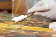 Close of gloved hands cleaning an old painting
