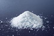 A close-up photograph of a heap of salt (sodium chloride) on a dark surface