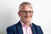 A photo of Declan McGeown, a man wearing a pink shirt, blue blazer and glasses.