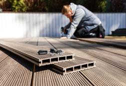 A man uses an electric drill and composite materials to make a decking area in a garden
