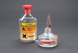 A glass bottle of ethanol labelled highly flammable and harmful with ethanol burning in a spirit burner
