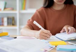 A student sitting at a desk, reading from a book while making notes