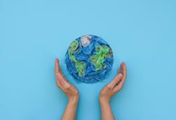 Two hands on either side of a circle of green and blue disposable plastic resembling the Earth