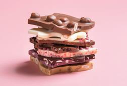 A close-up photograph of pieces of unusual chocolate bars with fruit, nuts and other ingredients in white, milk and dark chocolate