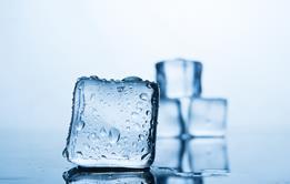 A close-up photograph of an ice cube melting against a neutral background with three more ice cubes visible behind it