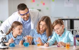 Teacher leaning over three learners who are pouring liquids into chemistry glassware.