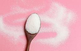 Sugar on a wooden spoon with a pink background