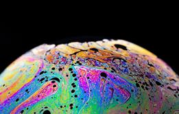 A close-up photograph of the surface of a soap bubble, multi-coloured against a black background
