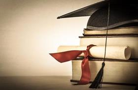 A mortarboard and diploma atop a pile of books