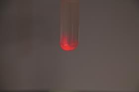 Red glow in a test tube on a grey background; demonstrating chemiluminescence