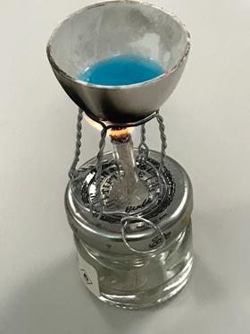 A mini fuel burner made from a miniature jam jar making blue copper sulfate crystals