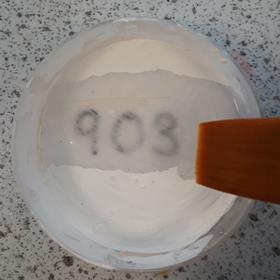 A paintbrush revealing a code in a petri dish covered with hydrochromic paint