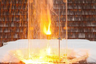 A sparks and bright flash of hot material in a terracotta flowerpot held in a laboratory clamp and stand. The set up is outside with some snow behind a protective clear screen