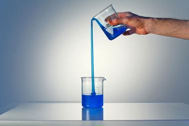 A glass beaker pouring liquid uphill into another