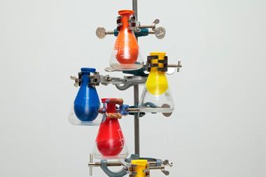 A number of glass conical flasks attached by clamps to a metal stand. Each flask has a colourful balloon sealed around its neck that has been sucked inside the flask.