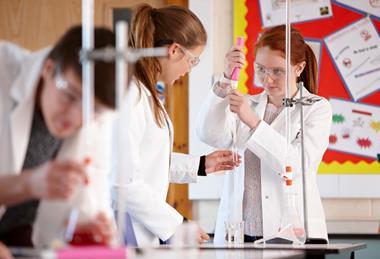 Students in a school lab using a burette filler to measure liquid for a titration