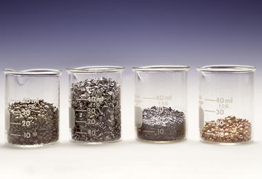 Four glass beakers holding different volumes of different metals 