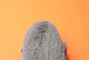 A close-up photograph of a pad of steel wool against an orange background