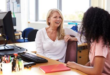 Photo of two ladies sitting at a desk and having a conversation