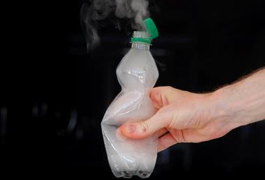 A hand squeezing a plastic bottle with vapour emerging from the neck