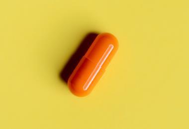 A photograph of an orange capsule pill on a yellow background