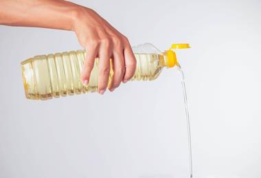 A photograph of somebody's hand pouring cooking oil from a plastic bottle against a white background