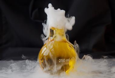 A conical flask of yellow liquid bubbles with a heavy white smoke