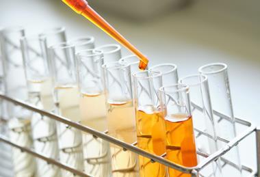 A photograph of a pipette held above test tubes in a metal test tube rack, containing different concentrations of an orange solution