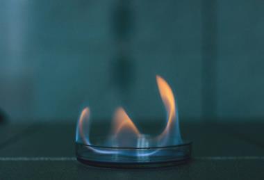 A photograph of ethanol burning with a blue, yellow and orange flame in a glass dish against a dark background