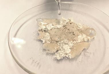 A photograph of calcium carbonate in a glass dish; as acid is dropped onto it using a pipette, producing carbon dioxide